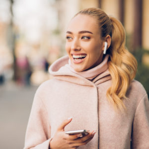 Stylish woman listening music on her airpods, walking in city at autumn day
